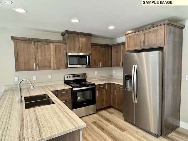 kitchen with a sink, light wood-style flooring, stainless steel appliances, and light countertops