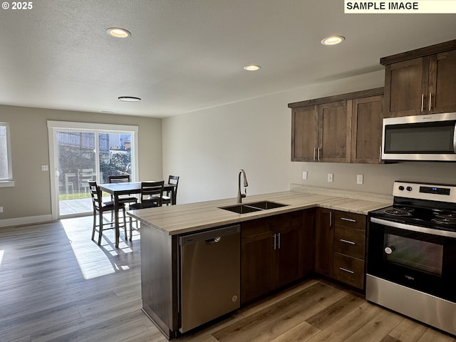 kitchen featuring appliances with stainless steel finishes, a peninsula, light countertops, dark brown cabinets, and a sink