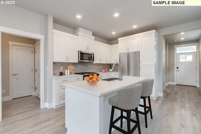 kitchen featuring appliances with stainless steel finishes, white cabinetry, an island with sink, sink, and light hardwood / wood-style flooring