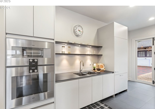 kitchen featuring double oven, tasteful backsplash, sink, white cabinets, and dark tile patterned floors