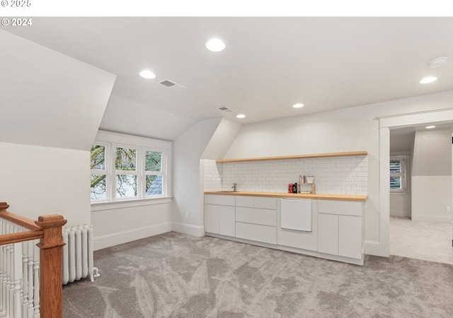 interior space with vaulted ceiling, radiator heating unit, sink, white cabinets, and light carpet