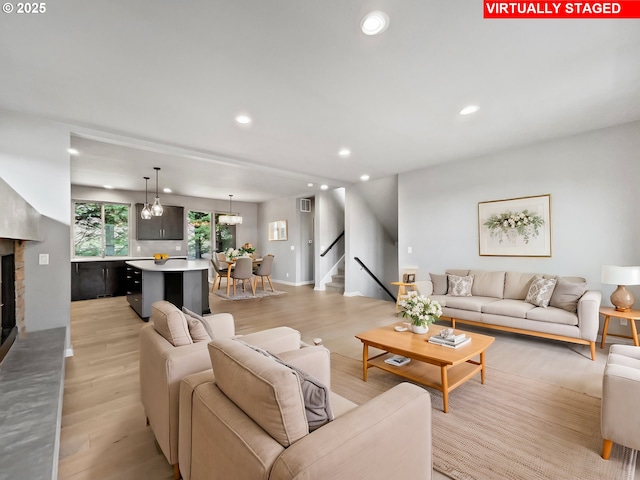 living room with a fireplace with raised hearth, recessed lighting, stairway, light wood finished floors, and a chandelier