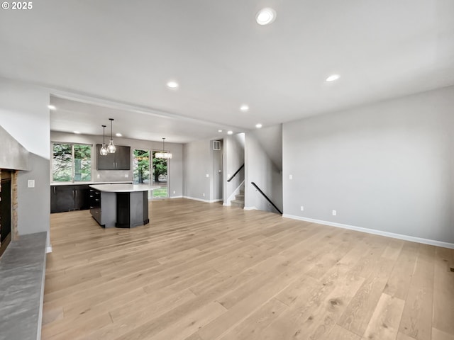 unfurnished living room with light wood finished floors, stairway, recessed lighting, a fireplace, and a notable chandelier