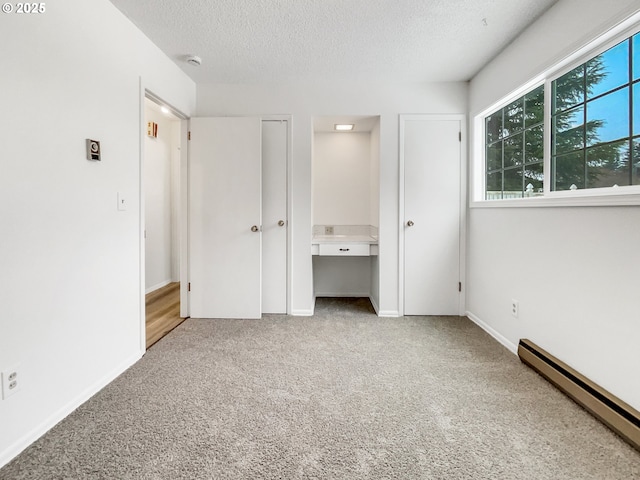 unfurnished bedroom with a baseboard heating unit, multiple closets, a textured ceiling, and carpet flooring