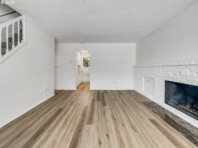 unfurnished living room featuring a textured ceiling, stairway, a fireplace, light wood finished floors, and baseboards