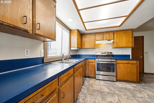 kitchen featuring dark countertops, appliances with stainless steel finishes, brown cabinetry, a sink, and under cabinet range hood