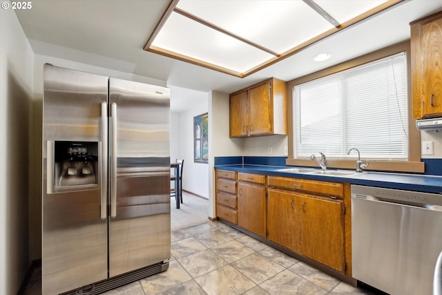 kitchen featuring appliances with stainless steel finishes, brown cabinetry, dark countertops, and a sink