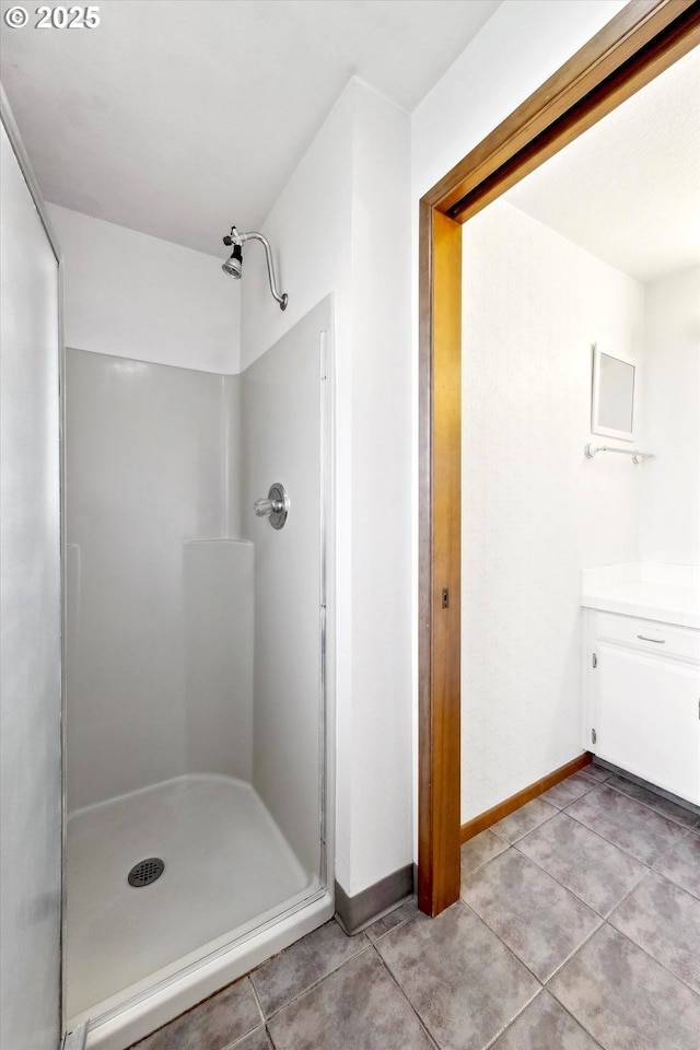 full bathroom with a stall shower, tile patterned flooring, vanity, and baseboards