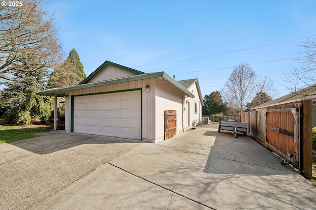 view of side of property featuring an outbuilding, concrete driveway, an attached garage, central AC, and fence