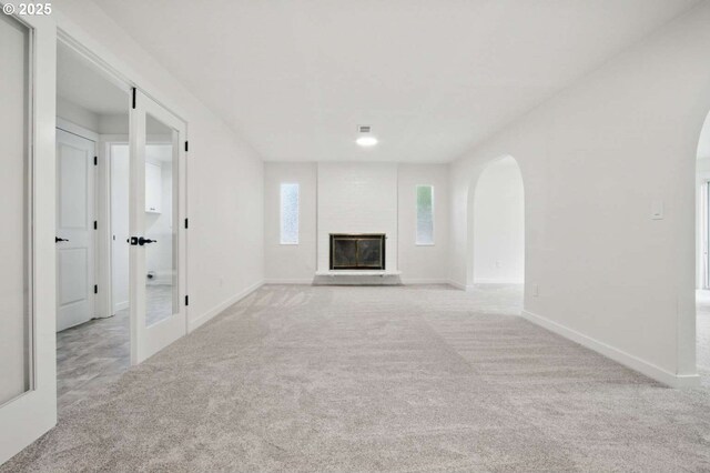 unfurnished living room with carpet floors, arched walkways, baseboards, and a glass covered fireplace