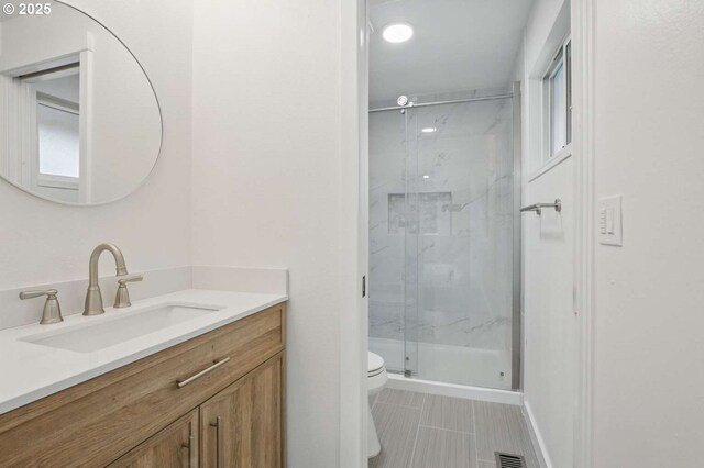 bathroom featuring toilet, a marble finish shower, vanity, and tile patterned flooring