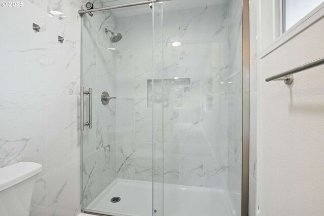 bathroom with toilet and a marble finish shower