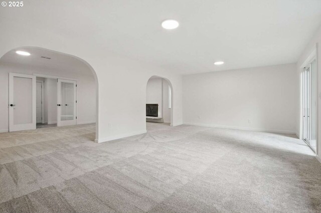 unfurnished room featuring arched walkways, light carpet, recessed lighting, and baseboards