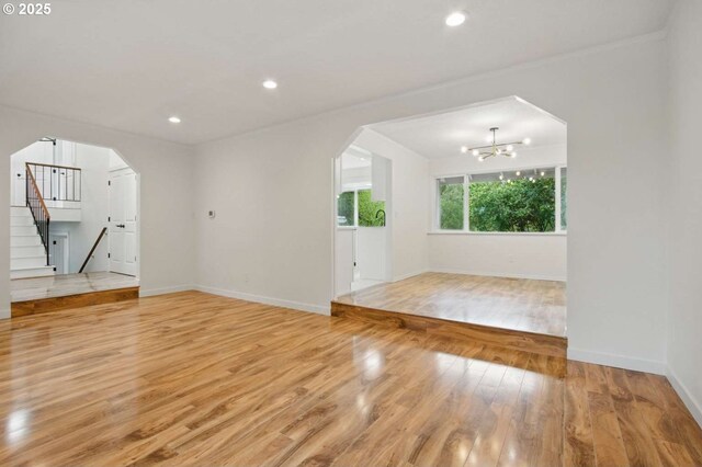 spare room featuring arched walkways, light wood finished floors, stairway, a chandelier, and baseboards