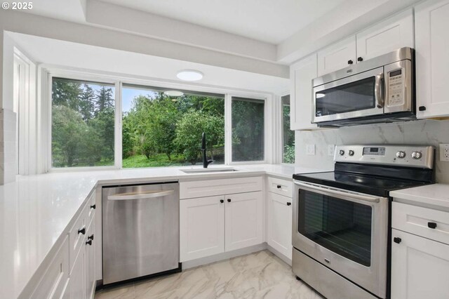 kitchen featuring stainless steel appliances, a sink, light countertops, white cabinetry, and light marble finish floors