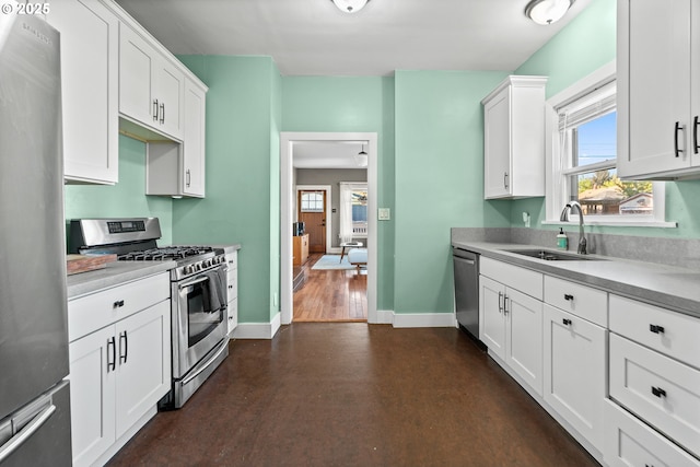 kitchen with stainless steel appliances, a sink, baseboards, and white cabinetry