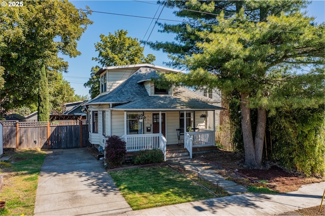 bungalow-style home with covered porch, fence, a shingled roof, and driveway
