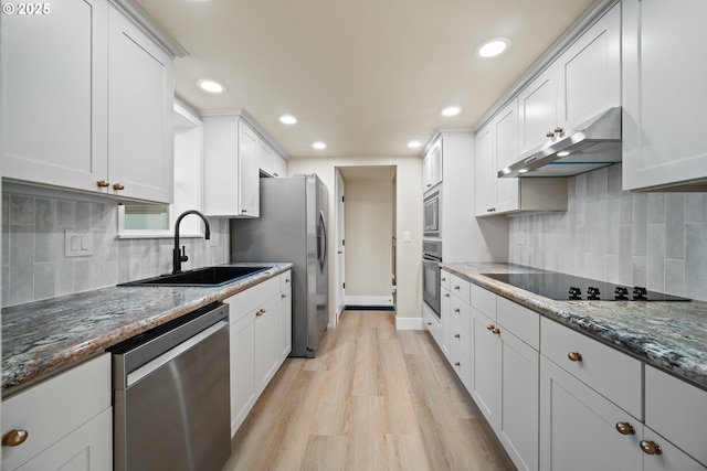 kitchen featuring dark stone countertops, white cabinets, stainless steel appliances, and light wood-type flooring