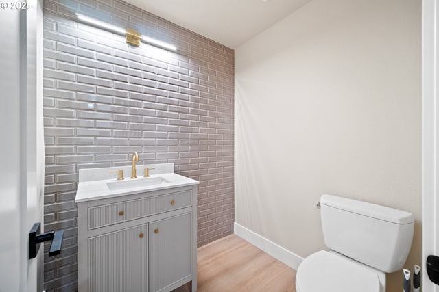 bathroom with vanity, toilet, wood-type flooring, and brick wall