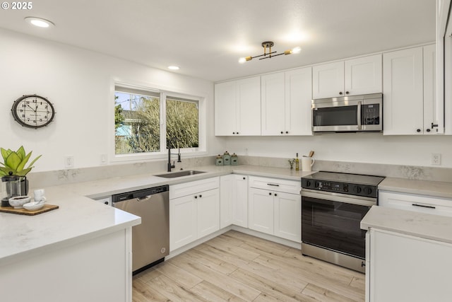 kitchen with sink, appliances with stainless steel finishes, light stone countertops, light hardwood / wood-style floors, and white cabinets