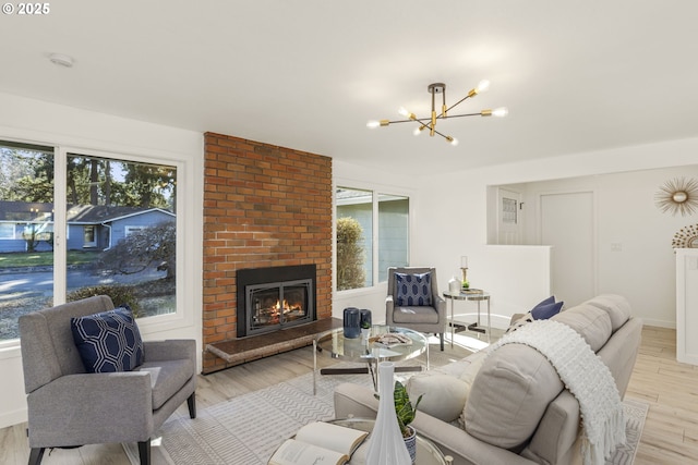 living room with a brick fireplace, a chandelier, a wealth of natural light, and light wood-type flooring