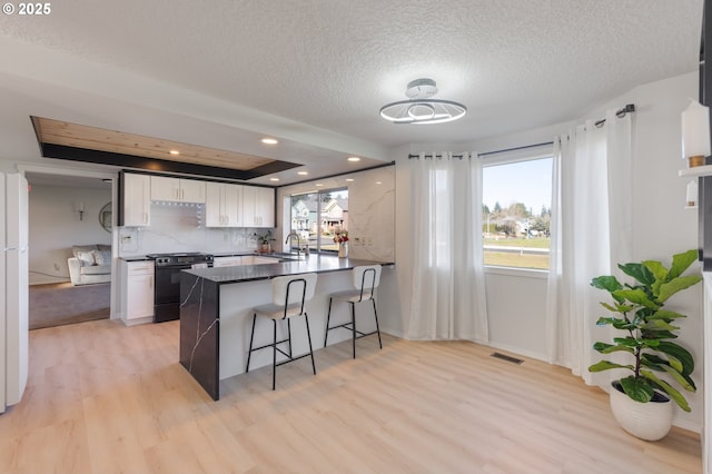 kitchen with sink, white cabinetry, black stove, kitchen peninsula, and light wood-type flooring