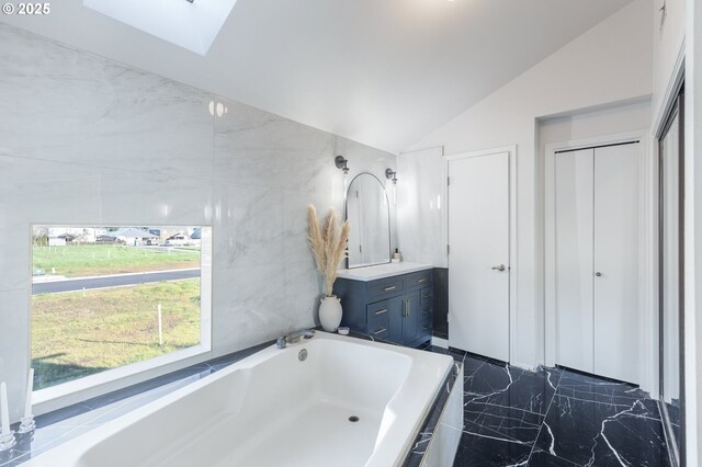 bathroom featuring vanity, a relaxing tiled tub, and vaulted ceiling with skylight