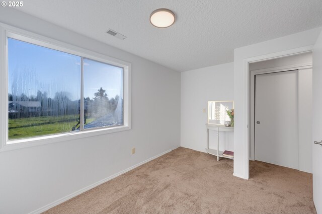 unfurnished bedroom featuring multiple windows, light carpet, and a textured ceiling