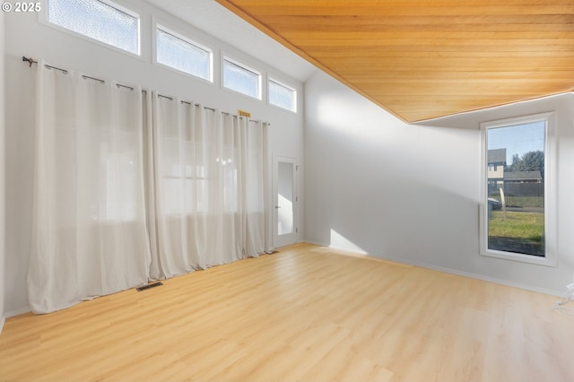 empty room with wood ceiling, light hardwood / wood-style flooring, and a high ceiling