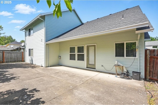 rear view of house featuring roof with shingles, fence, and a patio area