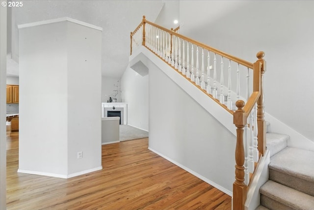 stairway featuring wood finished floors, a fireplace, a high ceiling, and baseboards