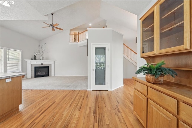 unfurnished living room featuring ceiling fan, light wood-style flooring, a tile fireplace, stairs, and high vaulted ceiling