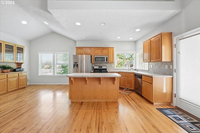 kitchen featuring stainless steel appliances, tile countertops, a center island, a sink, and light wood-style floors