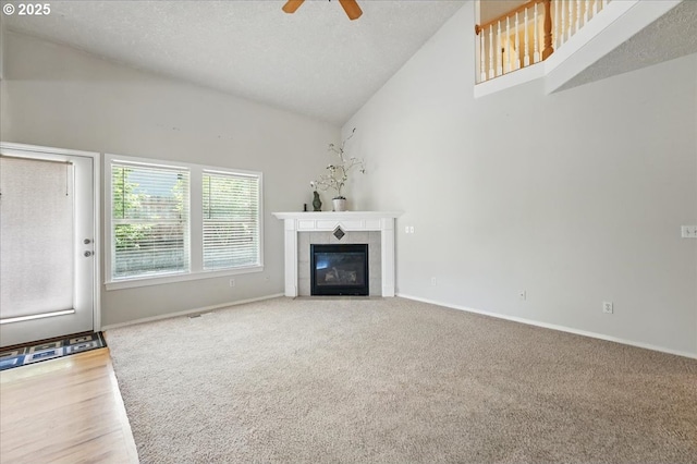 unfurnished living room featuring ceiling fan, a tiled fireplace, carpet flooring, high vaulted ceiling, and baseboards