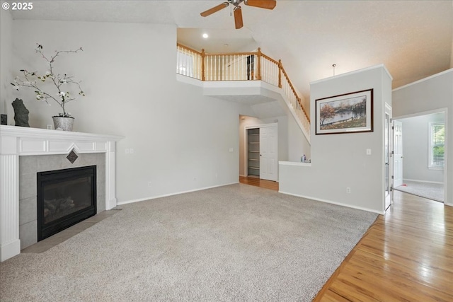 unfurnished living room featuring ceiling fan, stairway, a tile fireplace, baseboards, and light wood-type flooring