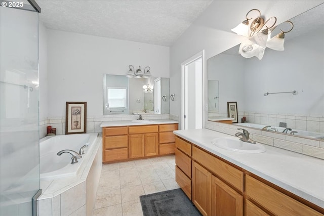 full bathroom featuring a chandelier, a textured ceiling, tile patterned floors, two vanities, and a garden tub
