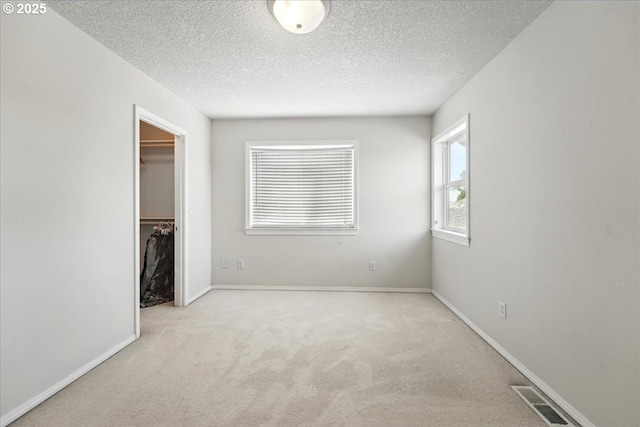 unfurnished bedroom featuring carpet, a textured ceiling, a walk in closet, baseboards, and a closet