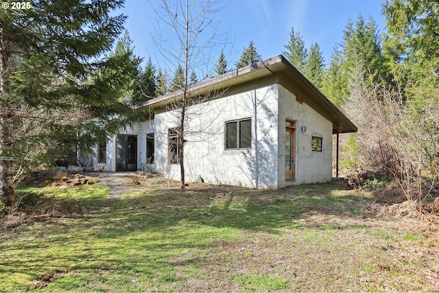 back of house featuring stucco siding and a yard