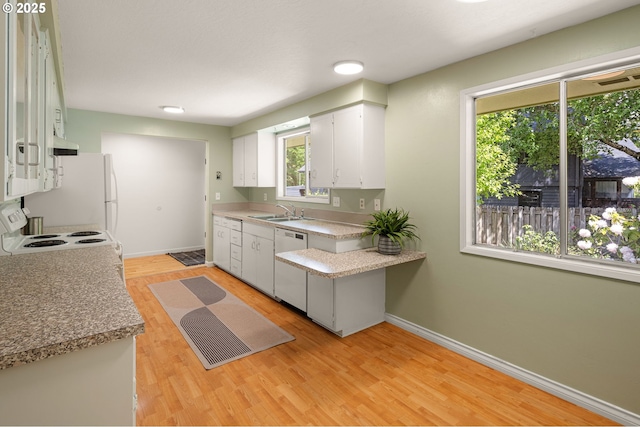 kitchen with a sink, white appliances, baseboards, white cabinetry, and light wood finished floors