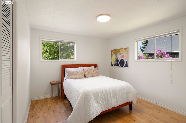 bedroom with light wood finished floors, multiple windows, and baseboards