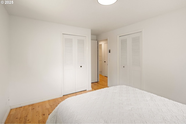 bedroom featuring two closets, light wood-type flooring, and baseboards