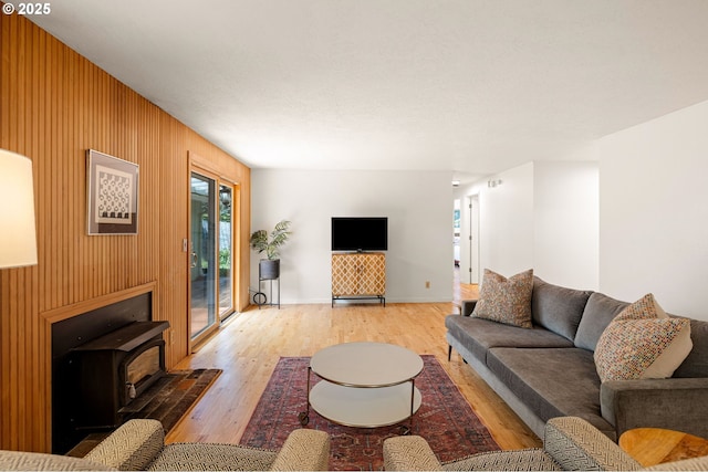 living room with wood finished floors, wood walls, a wood stove, and baseboards