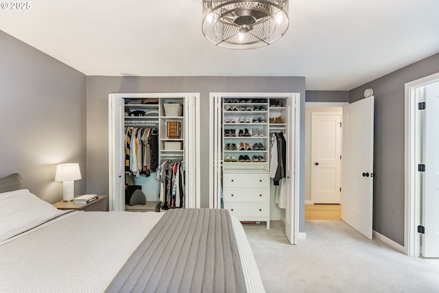 bedroom with two closets, light carpet, and baseboards