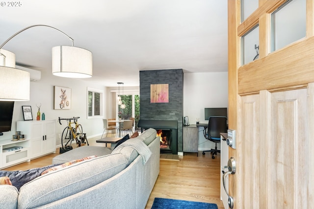 living area with light wood-style floors, an office area, a wall unit AC, and a fireplace