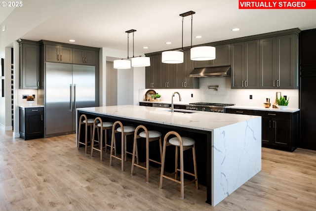 kitchen featuring light wood-type flooring, under cabinet range hood, stainless steel built in fridge, and a sink