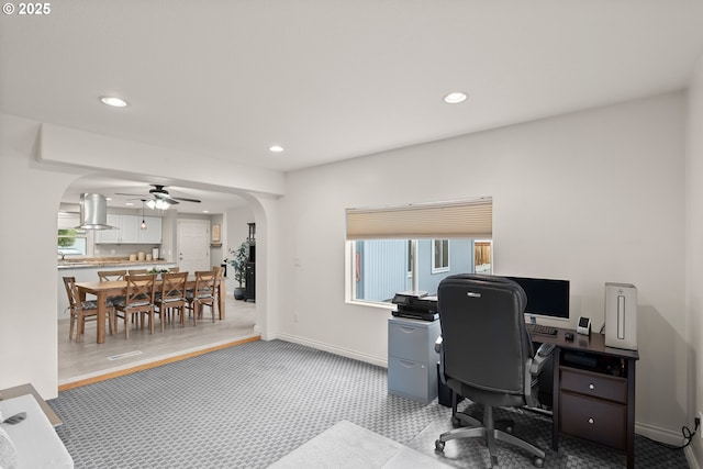 home office featuring a ceiling fan, baseboards, recessed lighting, arched walkways, and light carpet