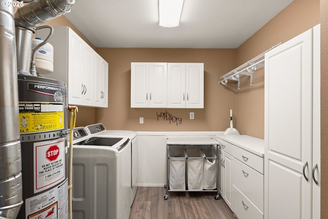 washroom featuring strapped water heater, light wood-style flooring, cabinet space, and washing machine and clothes dryer