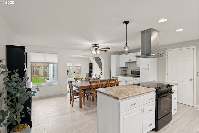 kitchen featuring stainless steel microwave, light countertops, island range hood, arched walkways, and electric range