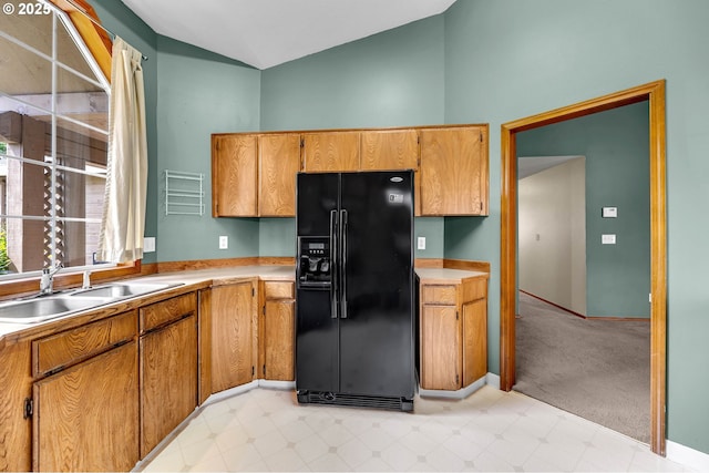 kitchen featuring brown cabinets, a sink, black refrigerator with ice dispenser, and vaulted ceiling