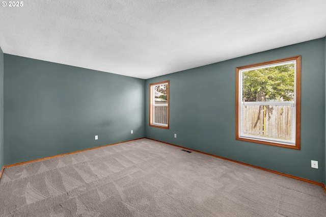 carpeted spare room featuring baseboards, visible vents, and a healthy amount of sunlight
